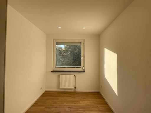 Büro/ Kinderzimmer/ Ankleide Leerer Raum mit Fenster, Fußboden aus Holz und Heizkörper unter dem Fenster.