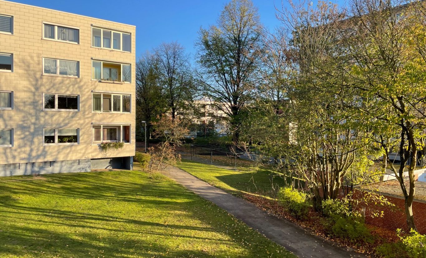 Außenansicht Wohnung in BS-Broitzem mit Garten Helle Wohnanlage mit roten Ziegeln, weißen Balkonen und einem blauen Himmel im Hintergrund.