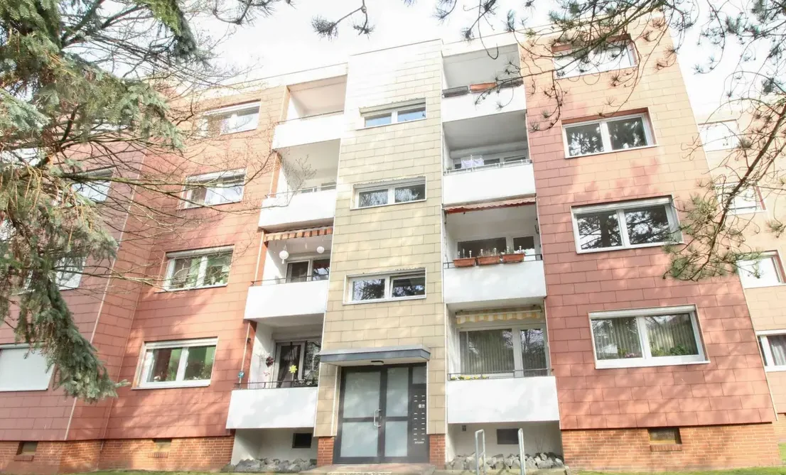 Außenansicht Wohnung in BS-Broitzem mit Garten Helle Wohnanlage mit roten Ziegeln, weißen Balkonen und einem blauen Himmel im Hintergrund.